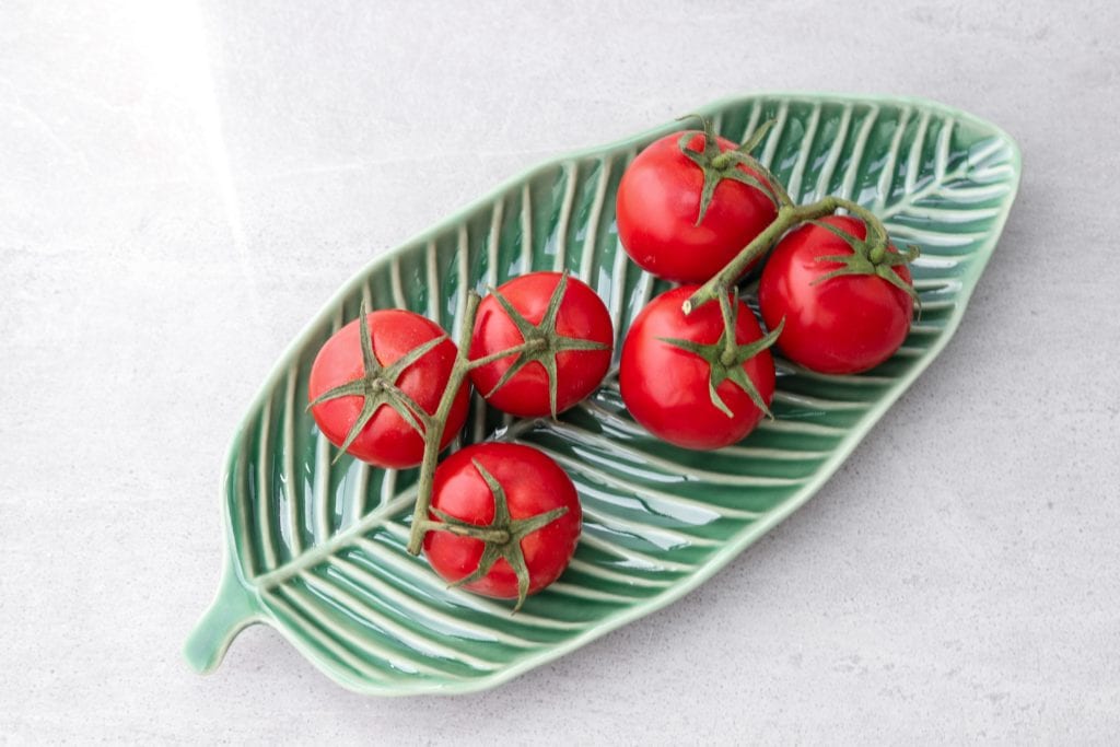 6 cherry tomatoes on a leaf-shaped dish on white background