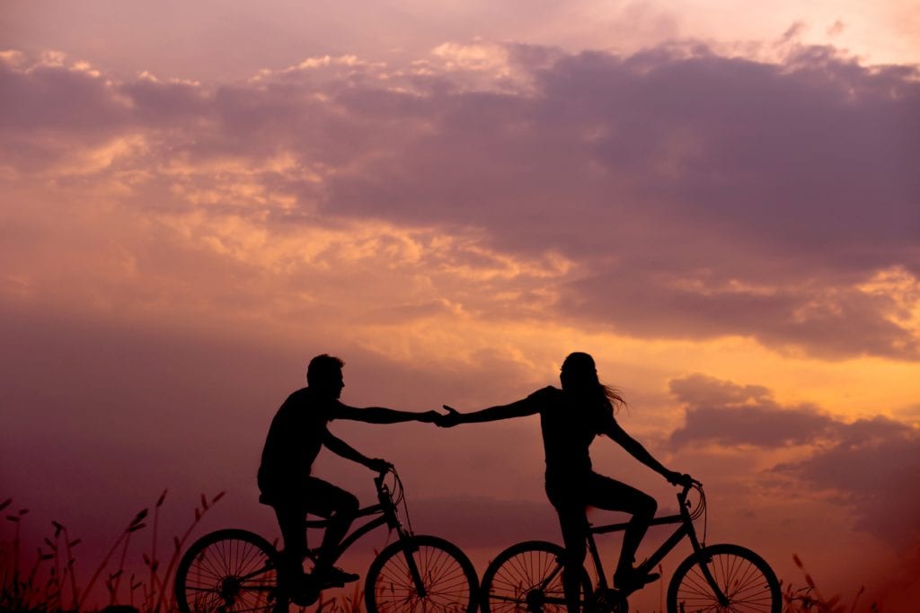 couple on bikes at sunset touching hands