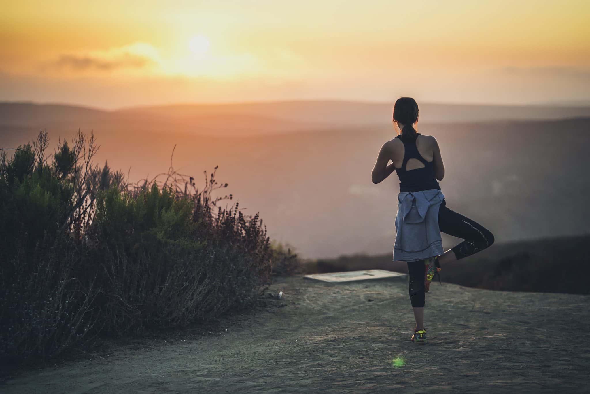 woman doing yoga on a hill at sunrise