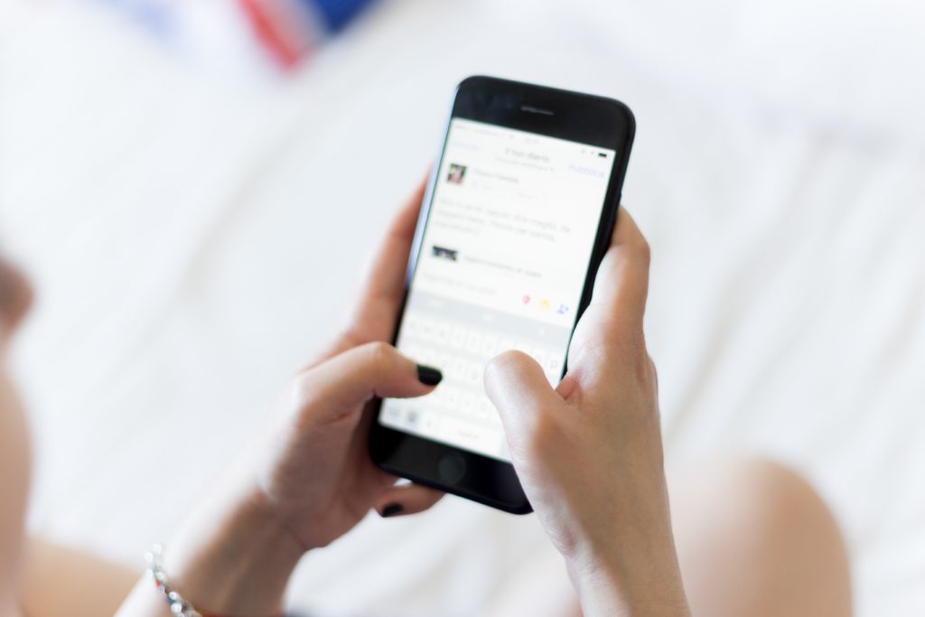person holding smartphone sitting on a bed