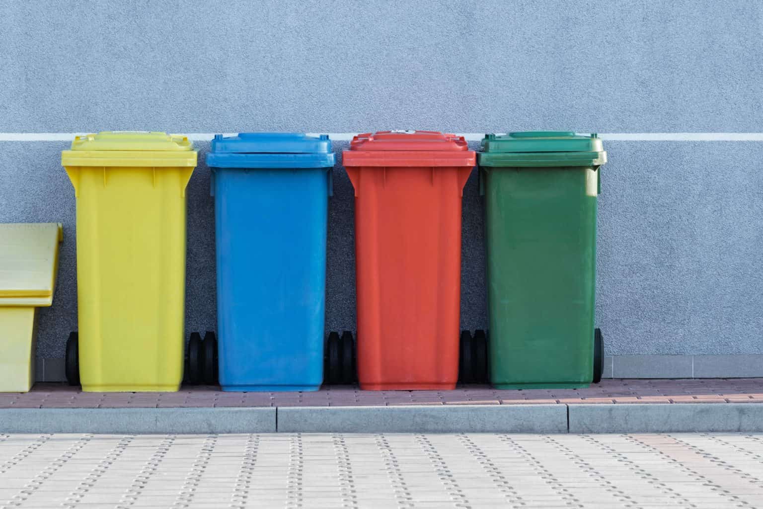 yello, blue, red and green waste bins lined up outside against a wall