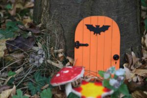 orange fairy door and mini flowers and toadstools against a tree trunk