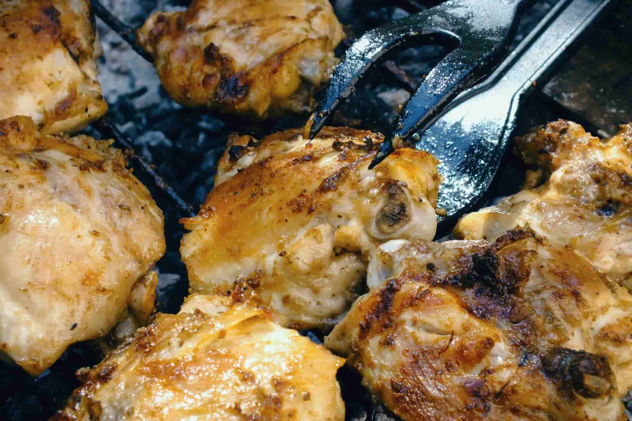 chicken being grilled on a BBQ with tongs in shot