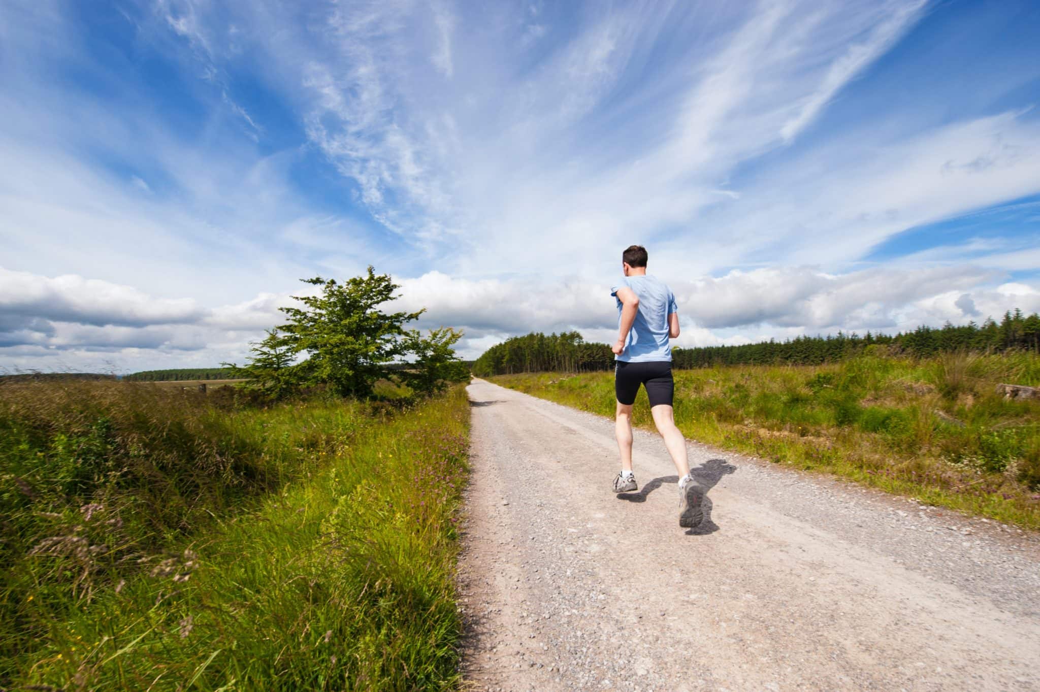 man running along long straight gravel path with grass either side
