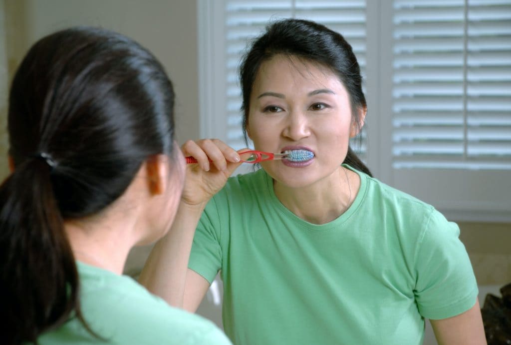 lady in green t shirt brushing teeth in mirror