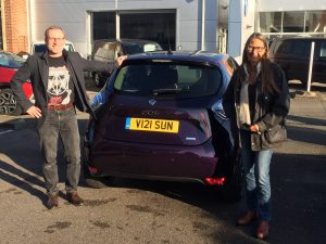 Lars and Helene standing to the rear of their purple electric car, smiling happily with their purchase