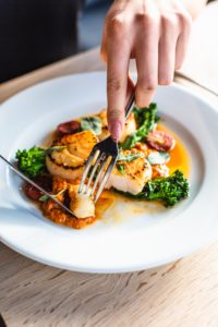 someone eating a plaste of scallops with broccoli on a white plate