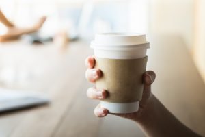 how to recycle coffee cups and sleeves - person holding a coffee cup