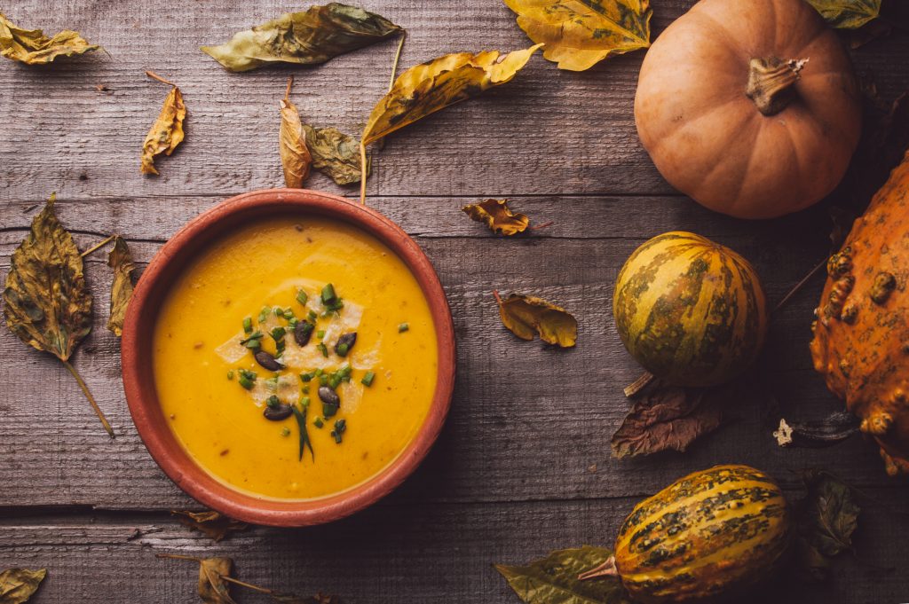 PUmpkin soup in a bowl, surrounded by autumn leaves and pumpkins