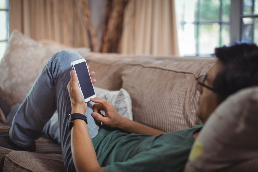 man laying on a sofa scrolling the news on his phone