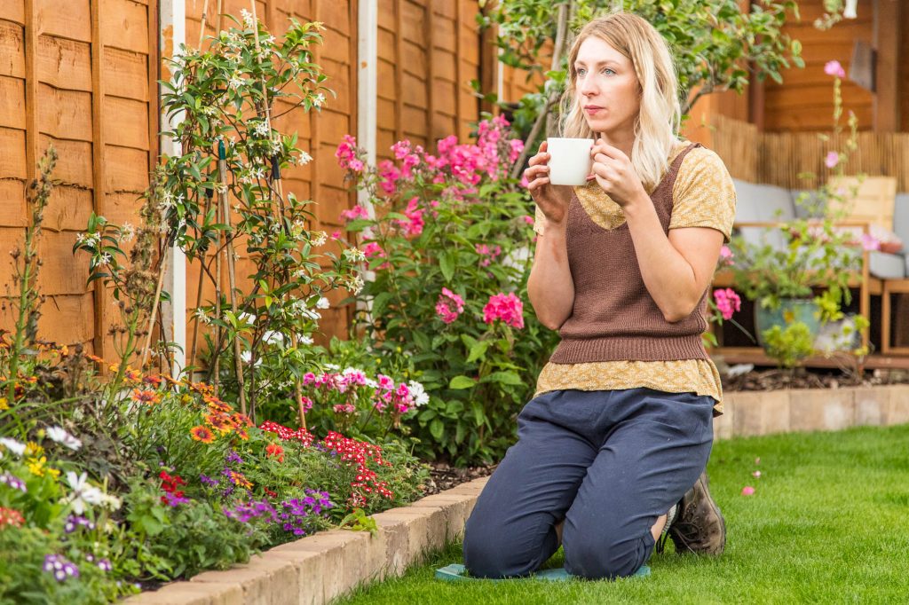 sarah kneeling in her garden with a cup of tea, contemplating the benefits of gardening for mental health