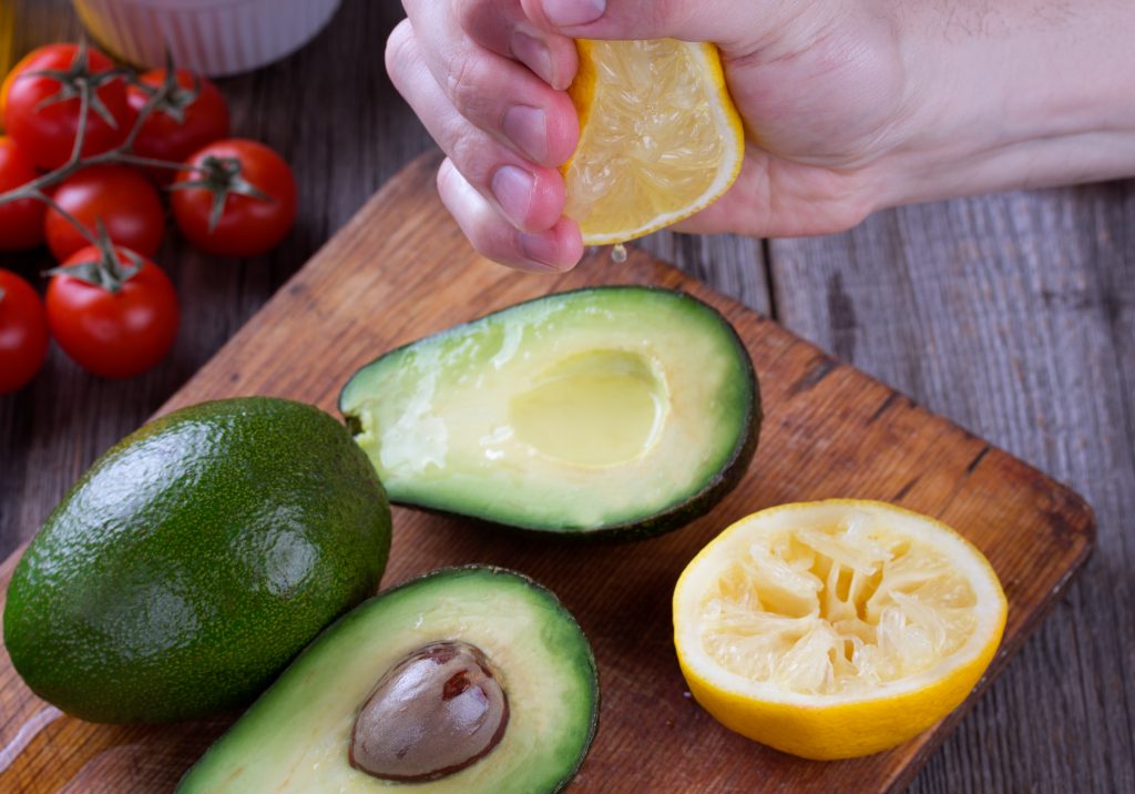 Someone using a lemon to stop avocados from browning by squeezing on the juice