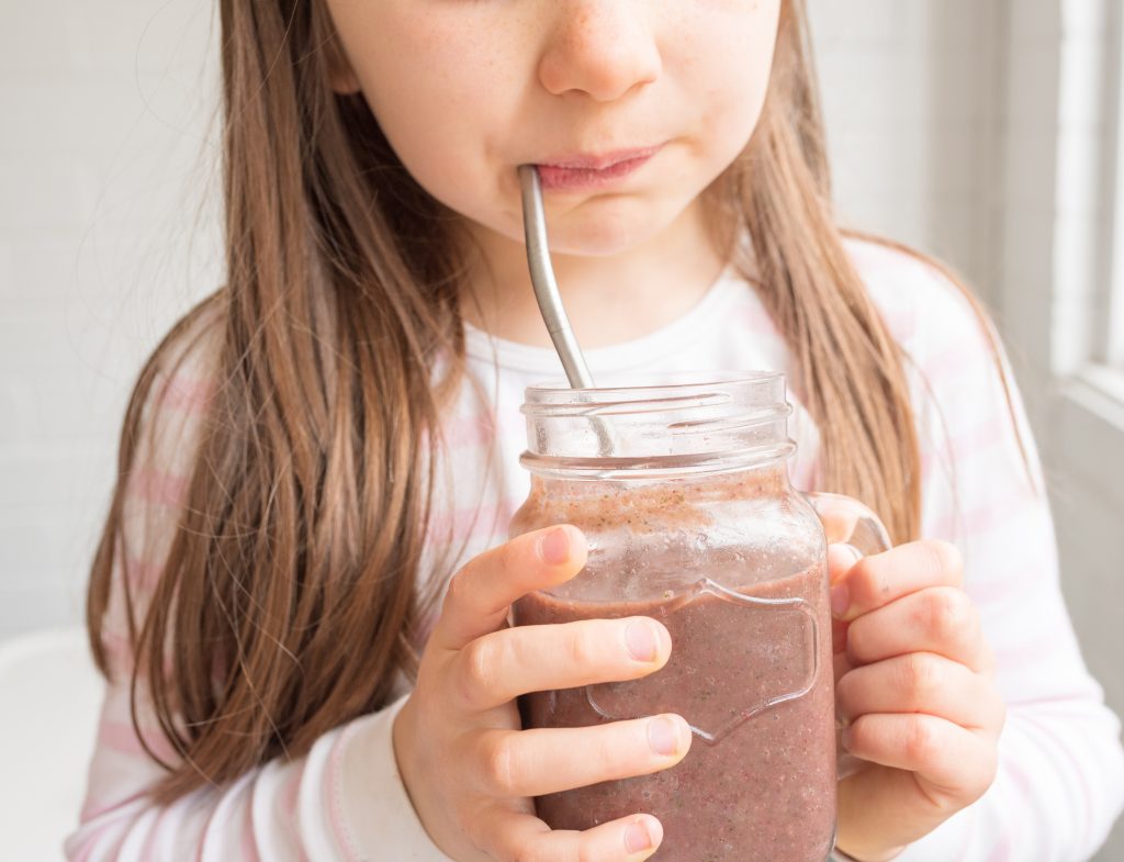 A young girl drinking from a glass jar through a metal straw