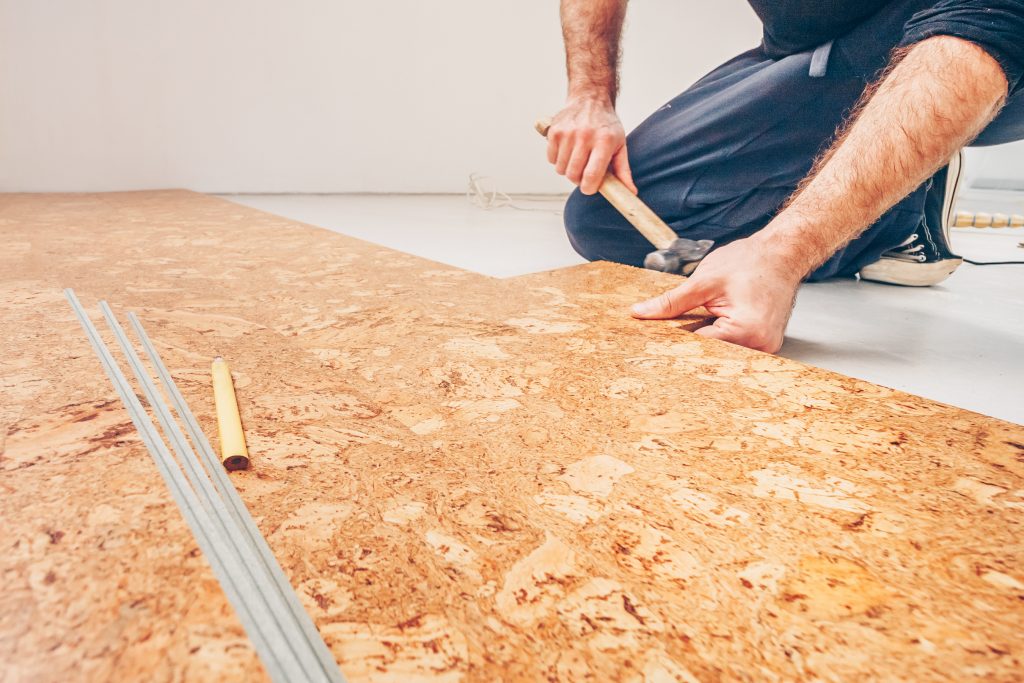 someone laying cork flooring, which is much more eco-friendly than traditional floors when decorating your home